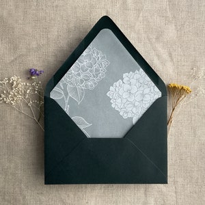 May include: A black envelope with a white floral design on the inside. The design features two hydrangeas with leaves.