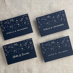 May include: Four navy blue cards with white constellation designs and the text "Stella K. December" printed on each card.