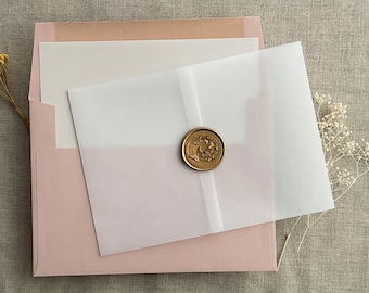 Può includere: Una busta rosa chiaro contenente un cartoncino color crema, coperto da un involucro in carta velina traslucida fissato con un sigillo di ceralacca circolare color bronzo con un motivo a farfalla in rilievo, accompagnato da rametti di fiori bianchi secchi.