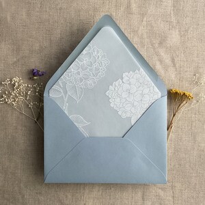 Pu&ograve; includere: Una busta blu chiaro con un disegno floreale bianco sul davanti. La busta &egrave; realizzata in carta testurizzata e ha un leggero bagliore.