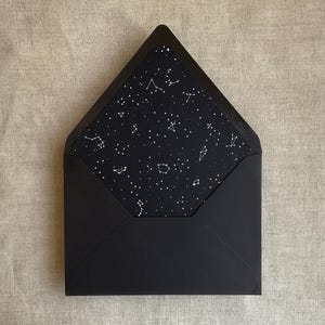 May include: A black envelope with a celestial design. The interior features a black background with white constellations and stars. The envelope is open, revealing the patterned interior.