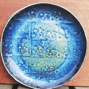 May include: A blue ceramic plate with a white glaze and a pattern of small, white flowers. The plate has a rustic, handmade look.