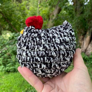 May include: A black and white crocheted chicken toy with a red comb and yellow beak.