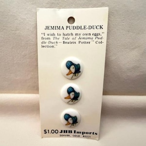 May include: A card featuring three Jemima Puddle-Duck buttons. Each button has a white background with a blue and yellow duck illustration. The card includes text from Beatrix Potter's story and the text "JHB Imports, Denver, Colo 80231".