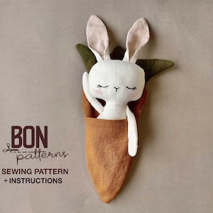 Könnte beinhalten: Ein weißes Stoffkaninchen mit rosa Ohren schaut aus einer braunen Karotte. Die Karotte hat grüne Blätter. Der Text "BON patterns SEWING PATTERN + INSTRUCTIONS" ist auf der linken Seite aufgedruckt.