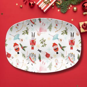 May include: White oval serving platter with a festive Nutcracker-themed pattern. The design includes illustrations of ballerinas, nutcrackers, and archers, along with sprigs of mistletoe and snowflakes. The platter is surrounded by Christmas decorations.