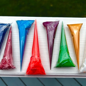 May include: Eight paint tubes in various colors, including red, orange, yellow, green, blue, purple, and white, are arranged in a row on a white surface. The tubes are all pointed towards the right side of the image.