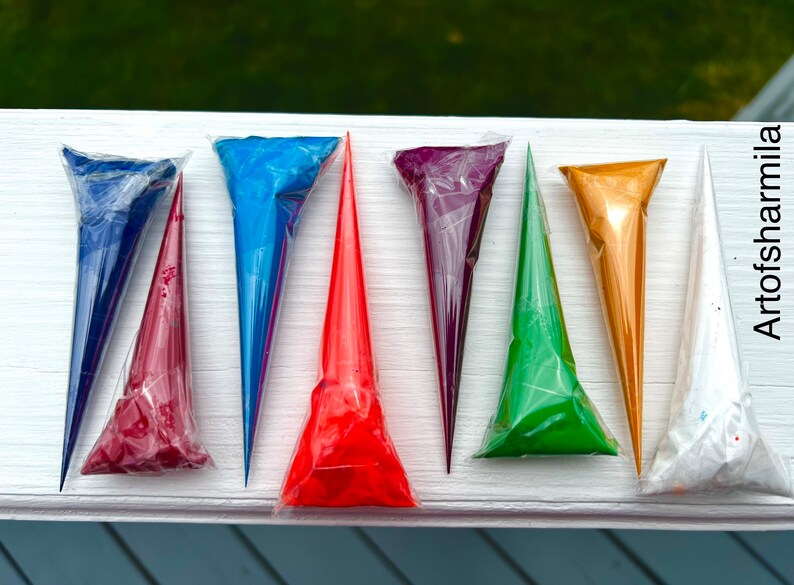 May include: Eight paint tubes in various colors, including red, orange, yellow, green, blue, purple, and white, are arranged in a row on a white surface. The tubes are all pointed towards the right side of the image.