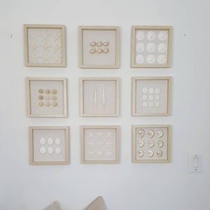 May include: Nine framed wall art pieces featuring various seashells and starfish. Each piece is encased in a light wood frame. The collection includes starfish, sand dollars, and various shell types, creating a coastal theme.