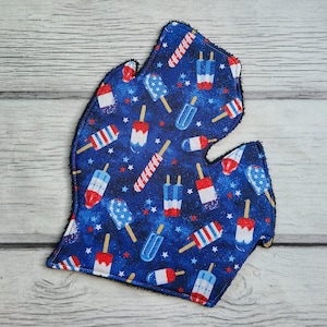 Puede incluir: Un agarrador de olla de tela azul con forma del estado de Michigan con un patrón de paletas de hielo rojas, blancas y azules sobre un fondo azul con estrellas blancas.
