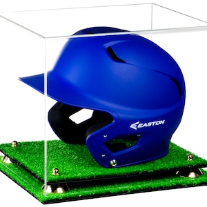 May include: A blue baseball helmet with a black face mask and the word "EASTON" on the side, displayed in a clear acrylic display case with a green grass base.