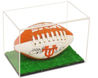 May include: A white and orange football with black laces and a signature on the side. The football is in a clear acrylic display case with a green grass base. The signature reads "Heath Shuler #21 Go Vols".