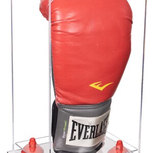 May include: A red Everlast boxing glove displayed inside a clear acrylic case. The glove is positioned upright, showcasing its red leather exterior and the Everlast logo. The case is supported by red suction cups.