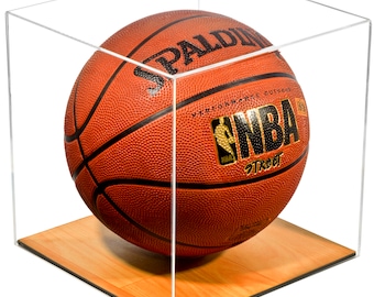 May include: A clear acrylic cube display case containing an orange Spalding NBA Street basketball. The case features a light brown wooden base with a printed basketball court floor pattern. The basketball has black seams and gold lettering.