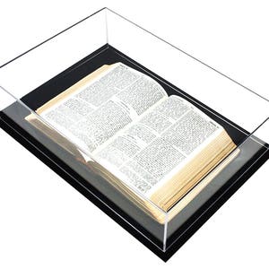 May include: A clear acrylic display case with a black base, showcasing an open book with aged pages.