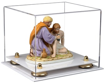 May include: A clear acrylic display case with a white base and gold accents. Inside the case is a porcelain figurine depicting a scene of two figures, one kneeling and the other sitting, with a brown jug on the ground.