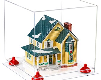 May include: A yellow and green miniature house with a white snowy roof sits inside a clear acrylic display case with four red plastic feet.