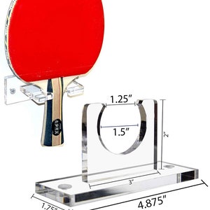 May include: A clear acrylic wall mount for storing a table tennis paddle. The mount is 4.875 inches wide, 3 inches long, and 2 inches tall. The paddle holder is 1.5 inches in diameter and 1.25 inches tall.