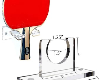 May include: A clear acrylic wall mount for storing a table tennis paddle. The mount is 4.875 inches wide, 3 inches long, and 2 inches tall. The paddle holder is 1.5 inches in diameter and 1.25 inches tall.
