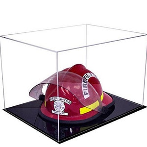 May include: A red firefighter helmet with a clear face shield and yellow reflective stripe, displayed inside a rectangular clear acrylic display case with a solid black base. The helmet features a white emblem with the text FIREFIGHTER FIRE DEPT.