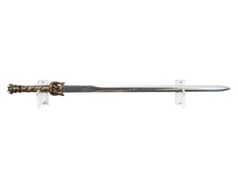 May include: A long, silver sword with an ornate, bronze-colored handle and guard. The sword is mounted on two clear acrylic brackets against a white background. The blade is straight and tapers to a point.