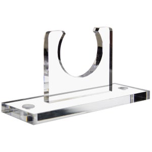 May include: Clear acrylic display stand with a circular cutout for holding a sword or other object. The stand has a rectangular base with two small screws on the bottom.