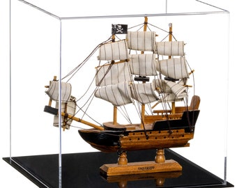 May include: A wooden model ship with black and natural wood hull, white striped fabric sails, and a black pirate flag with a skull and crossbones, enclosed in a clear acrylic display case with a black base. The base features the text ENGLEWOOD.