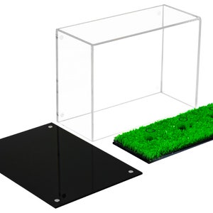 Op de afbeelding: Een transparante acryl vitrine met een zwarte basis en een groene kunstgras basis met drie gaten. De vitrine is ontworpen om kleine items te presenteren, zoals beeldjes of verzamelobjecten.