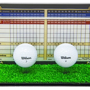 Op de afbeelding: Twee witte golfballen met zwarte Wilson-logo's en de nummers 3 en 4 erop zijn tentoongesteld in een doorzichtige acryl vitrine met een groene kunstgrasbasis. De vitrine heeft een scorekaart met nummers en een rasterpatroon. De scorekaart heeft de woorden "Blauw", "Wit" en "Rood" erop gedrukt.