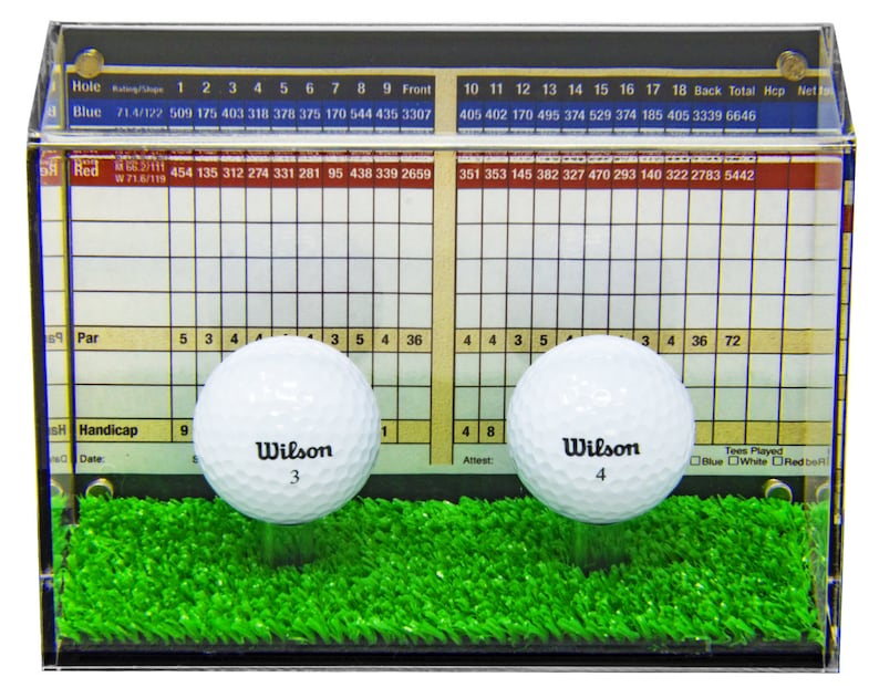 Op de afbeelding: Twee witte golfballen met zwarte Wilson-logo's en de nummers 3 en 4 erop zijn tentoongesteld in een doorzichtige acryl vitrine met een groene kunstgrasbasis. De vitrine heeft een scorekaart met nummers en een rasterpatroon. De scorekaart heeft de woorden "Blauw", "Wit" en "Rood" erop gedrukt.