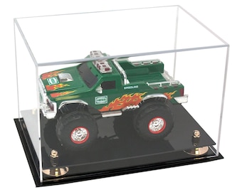 May include: A green toy truck with flames and the word "GASOLINE" on the side, displayed in a clear acrylic case with a black base.