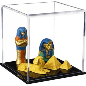 May include: A clear acrylic display case with a black base, showcasing a collection of Egyptian-themed figurines. The figurines include a pharaoh, a sphinx, and two pyramids, all painted in gold, blue, and green.