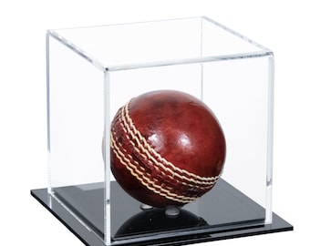 May include: A brown leather cricket ball with white stitching is displayed in a clear acrylic cube with a black base.