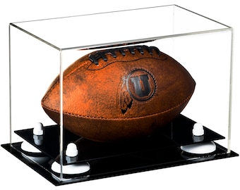 May include: A brown leather football with black laces and a black circular logo featuring the letter U, displayed inside a clear rectangular acrylic case. The case sits on a black base supported by four white circular risers with white caps.