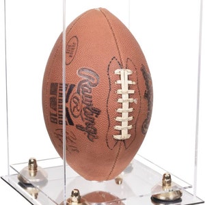May include: A brown leather football inside a clear acrylic display case. The football has white laces and black text. The case has a clear base with four gold-colored supports.
