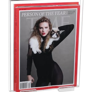 May include: Clear acrylic magazine holder displaying a TIME magazine cover. The cover features a person with long hair and red lipstick, holding a cat. The magazine is titled "PERSON OF THE YEAR" with the name "TAYLOR SWIFT".