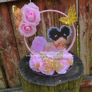 Pode incluir: Um topo de bolo com uma moldura circular rosa decorada com rosas de espuma rosa claro e tr&ecirc;s borboletas douradas met&aacute;licas. Um recorte de um beb&eacute; com cabelo encaracolado escuro e roupa rosa est&aacute; centrado, com o texto MyCurlyLove.