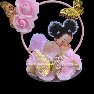 Pode incluir: Um topo de bolo com uma moldura circular rosa decorada com rosas de espuma rosa claro e borboletas met&aacute;licas douradas. Um recorte de um beb&eacute; com cabelo escuro encaracolado em marias-chiquinhas e roupa rosa com folhos est&aacute; centrado. Texto MyCurlyLove.