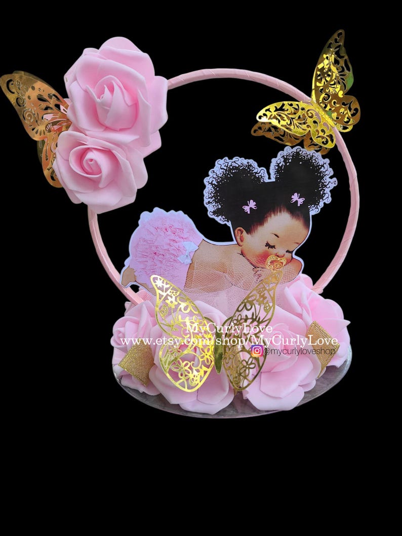 Pode incluir: Um topo de bolo com uma moldura circular rosa decorada com rosas de espuma rosa claro e borboletas met&aacute;licas douradas. Um recorte de um beb&eacute; com cabelo escuro encaracolado em marias-chiquinhas e roupa rosa com folhos est&aacute; centrado. Texto MyCurlyLove.
