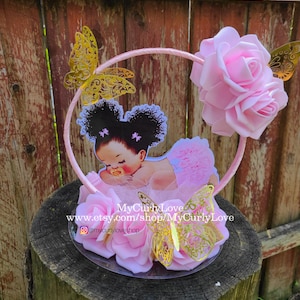 Pode incluir: Um centro de mesa decorativo com uma ilustra&ccedil;&atilde;o de beb&eacute; com cabelo escuro encaracolado e uma chupeta, rodeado por rosas de espuma cor-de-rosa e recortes de borboletas met&aacute;licas douradas numa moldura circular. Texto: MyCurlyLove www.etsy.com/shop/MyCurlyLove.