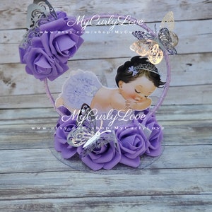 Pode incluir: Um centro de mesa decorativo com a ilustra&ccedil;&atilde;o de um beb&eacute; a dormir com uma tiara e uma saia com folhos, rodeado por rosas de espuma roxas e borboletas prateadas cortadas a laser numa moldura circular com o texto MyCurlyLove impresso.