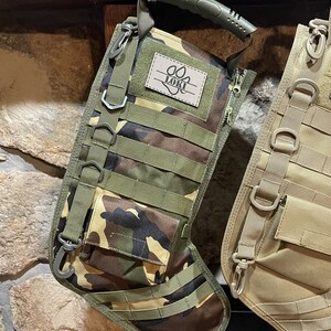 May include: Camouflage-patterned stocking with a black zipper and a green handle. The stocking has multiple straps and a patch with the name "Loki" and a paw print.