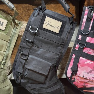 May include: Black tactical stocking with a zipper, a small pocket, and a handle. The stocking has a personalized name tag that says "Hannah".