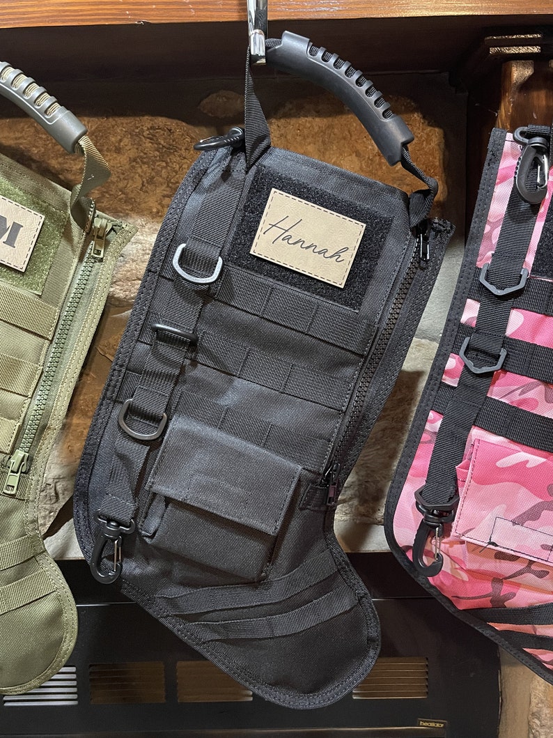 May include: Black tactical stocking with a zipper, a small pocket, and a handle. The stocking has a personalized name tag that says "Hannah".
