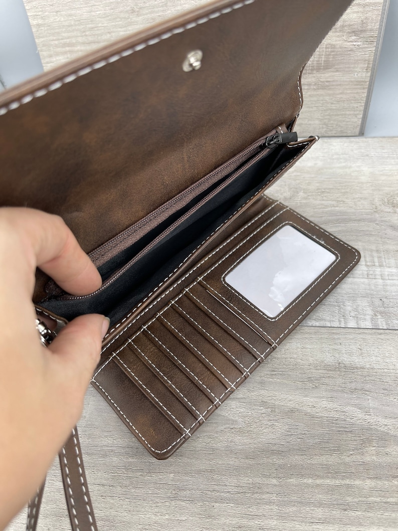 May include: A brown leather wallet with a zippered pocket and multiple card slots. The wallet has a white stitching detail and a clear plastic window for displaying an ID card.