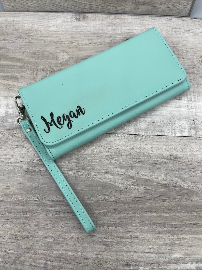 May include: A light blue leather wallet with a wrist strap. The wallet has the name "Megan" embossed on the front.