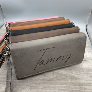 May include: A stack of five different colored leather wallets with a personalized inscription that reads "Tammy" on the gray wallet.