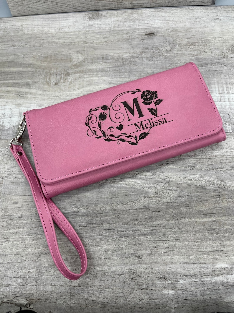 May include: A pink leather wallet with a black floral design and the letter "M" and the name "Melissa" engraved on the front.