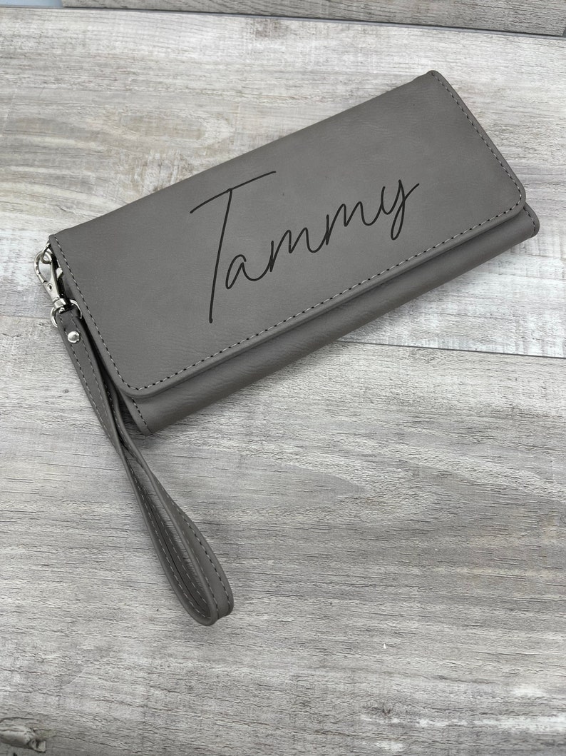 May include: A gray leather wallet with a wrist strap and the name "Tammy" engraved on the front.