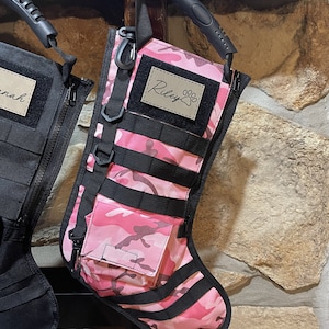 May include: Pink and black camouflage stocking with a black handle and a brown patch that says "Riley" with a paw print.